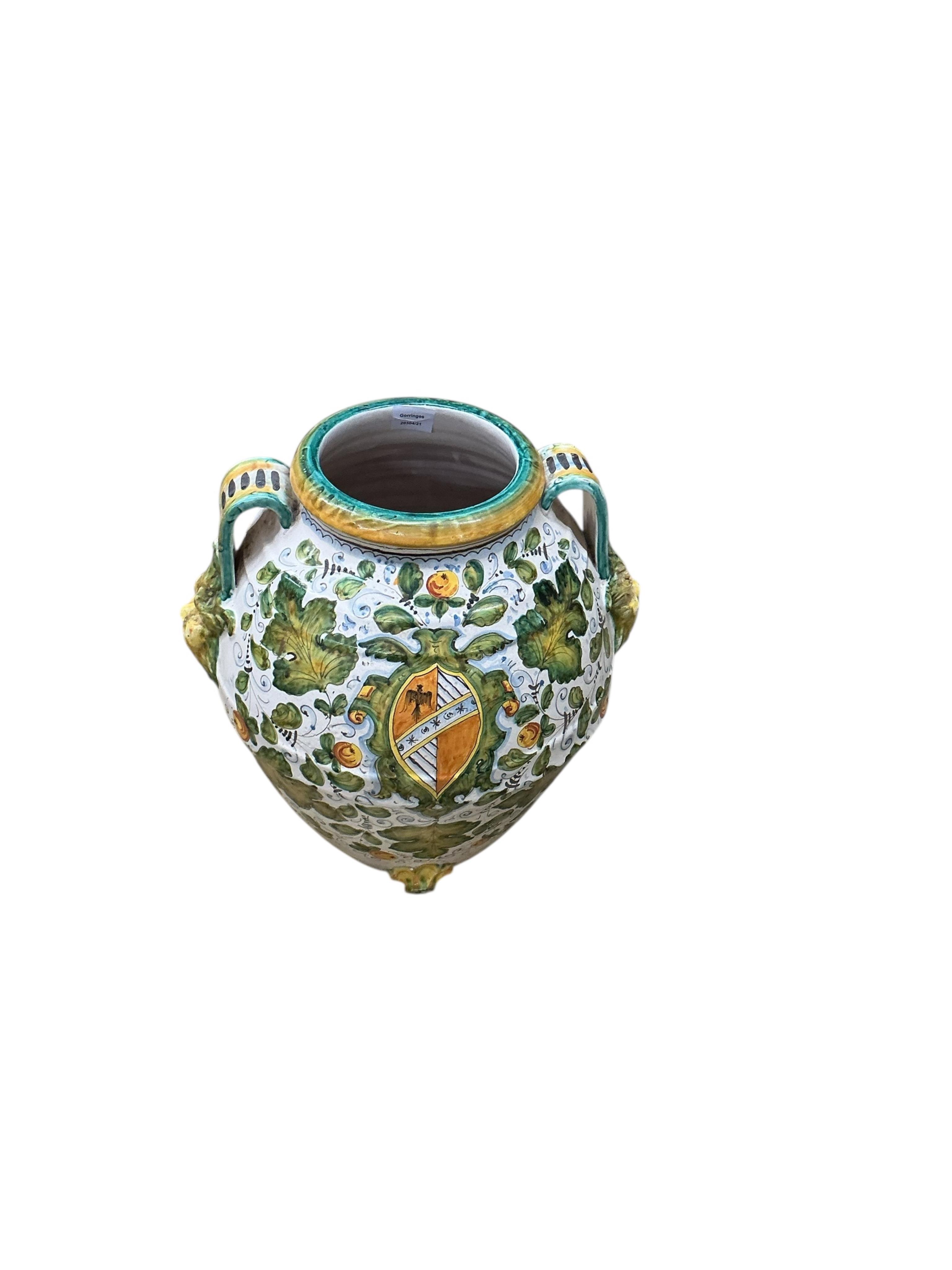 A large Italian Maiolica wine jar with spigot hole, twin handles with grotesque masks, all-over decorated with fruiting foliage and a central armorial cartouche, height 48cm